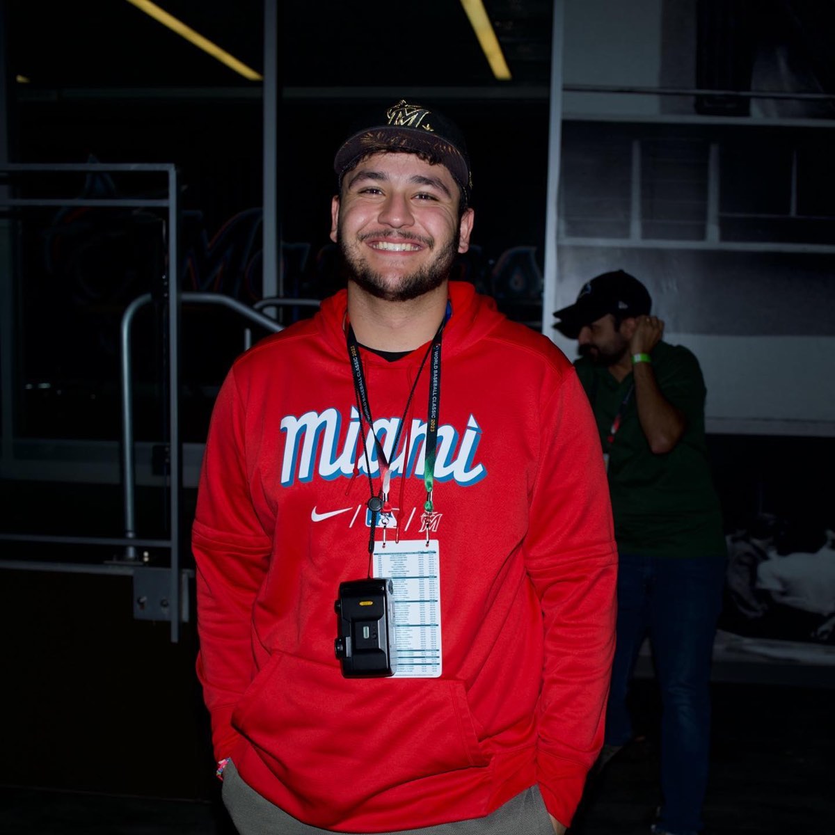 Julian Rosa in a red Miami hoodie and Marlins cap, with a camera and media credential